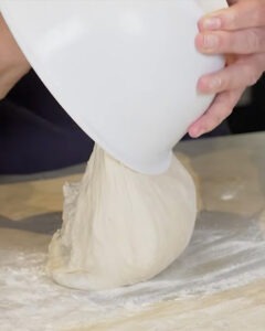 Hogaza de pan blanco con masa madre recién horneada junto a un bote de masa madre activa