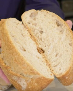 Hogaza de pan blanco con masa madre recién horneada junto a un bote de masa madre activa