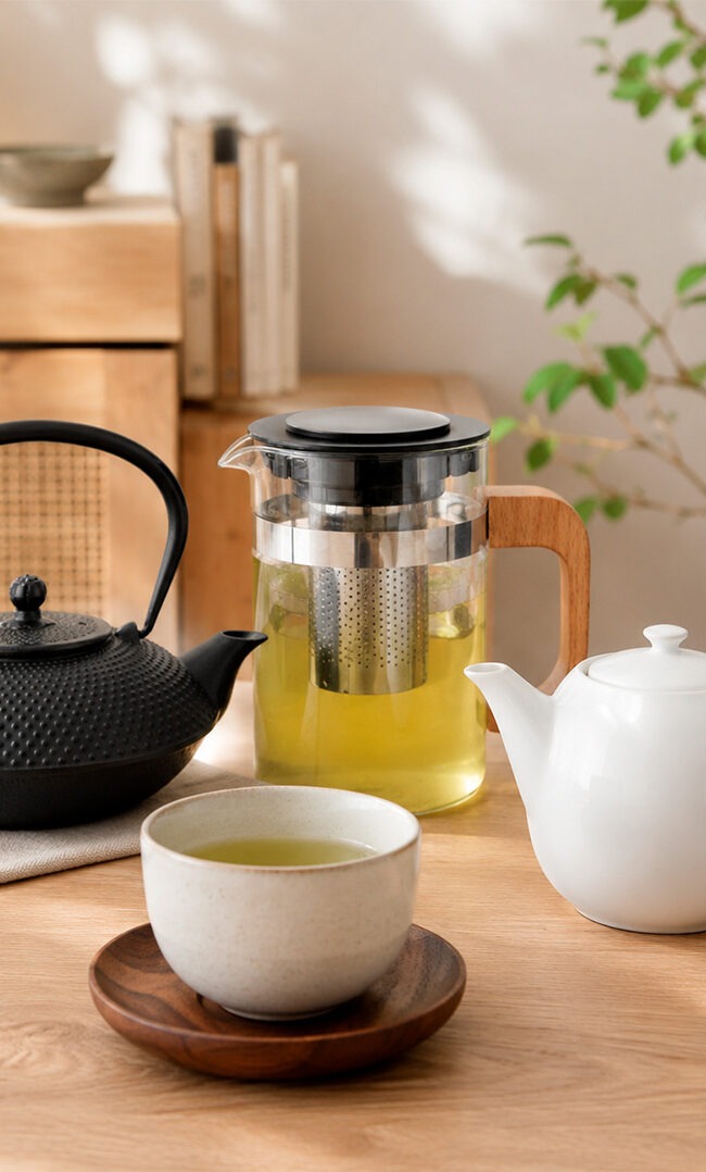 Tres teteras para infusiones: hierro negro Quid, cristal transparente Quid y porcelana blanca Prime Ariane, con sus respectivas tazas de té sobre mesa de madera