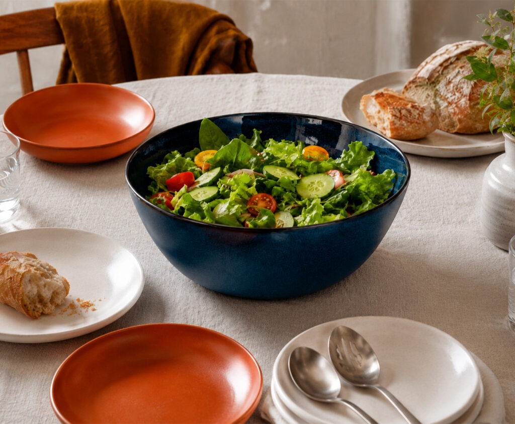 Ensaladera original de cerámica azul con ensalada de temporada en mesa de comedor bien puesta