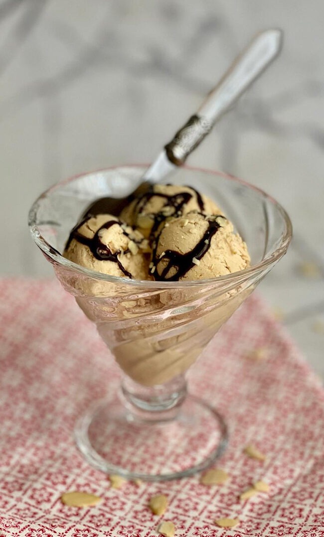 Helado de turrón de Jijona sin heladera servido en copa de cristal con chocolate negro y almendras sobre mármol blanco
