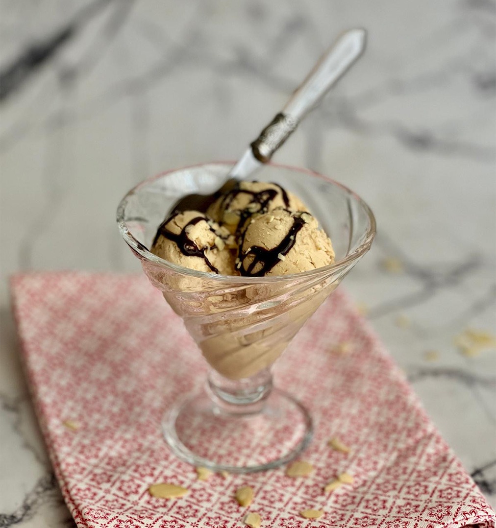 Helado de turrón de Jijona sin heladera servido en copa de cristal con chocolate negro y almendras sobre mármol blanco