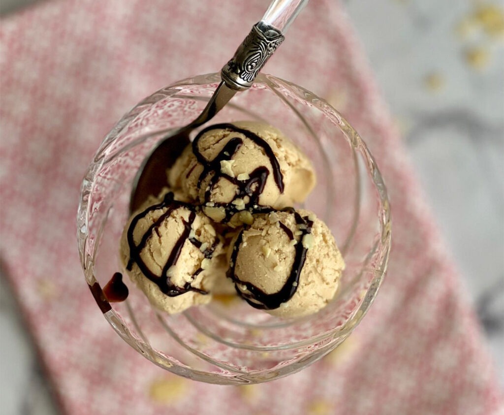 Helado de turrón de Jijona sin heladera servido en copa de cristal con chocolate negro y almendras sobre mármol blanco