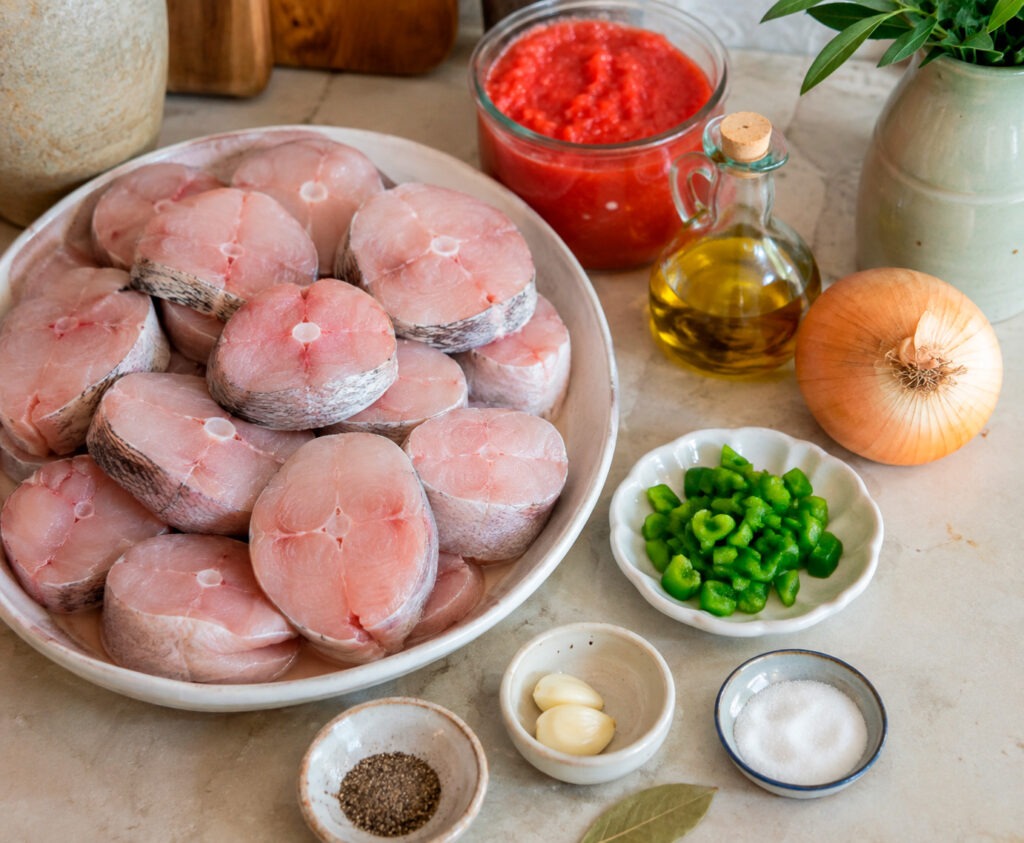 Cazón en tomate tradicional gaditano servido en plato hondo blanco con salsa de tomate espesa y pan al lado