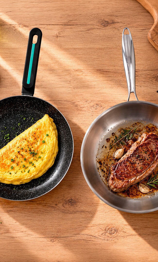 Sartén antiadherente con tortilla francesa junto a una sartén de acero inoxidable con un filete dorado