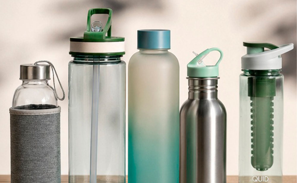 Botellas deportivas para gimnasio de vidrio plástico y acero sobre mesa con accesorios de entrenamiento