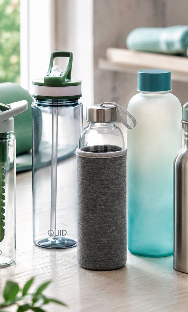 Botellas deportivas para gimnasio de vidrio plástico y acero sobre mesa con accesorios de entrenamiento
