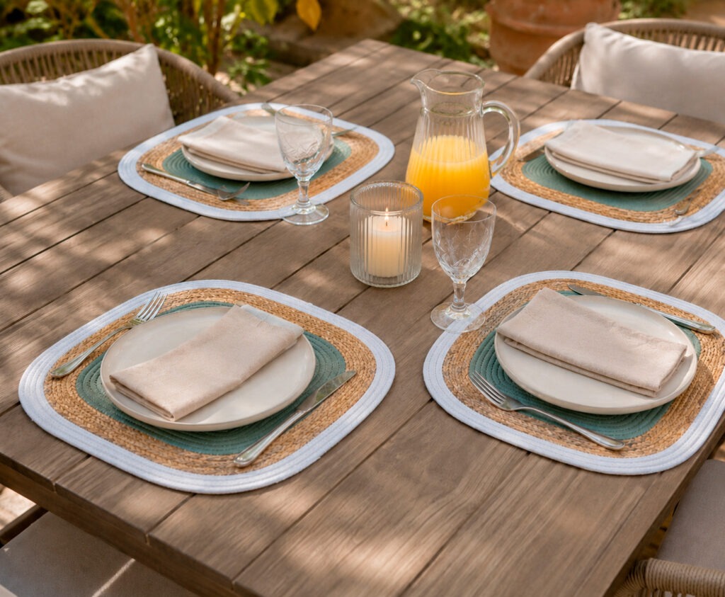 Mesa de comedor con manteles individuales redondos de rafia, vajilla blanca y vasos de cristal
